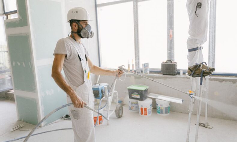 Two construction workers wearing protective gear and painting interior walls for a renovation project. - Photo by AI25.Studio Studio on Pexels