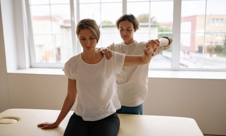 A therapist assists a woman with arm stretching during a physical therapy session in a bright, indoor setting. - Photo by Yan Krukau on Pexels