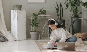 Asian woman seated on floor, using laptop and headphones, surrounded by indoor plants. - Photo by Pavel Danilyuk on Pexels
