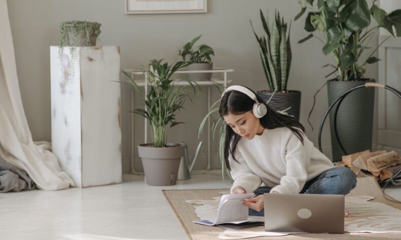 Asian woman seated on floor, using laptop and headphones, surrounded by indoor plants. - Photo by Pavel Danilyuk on Pexels